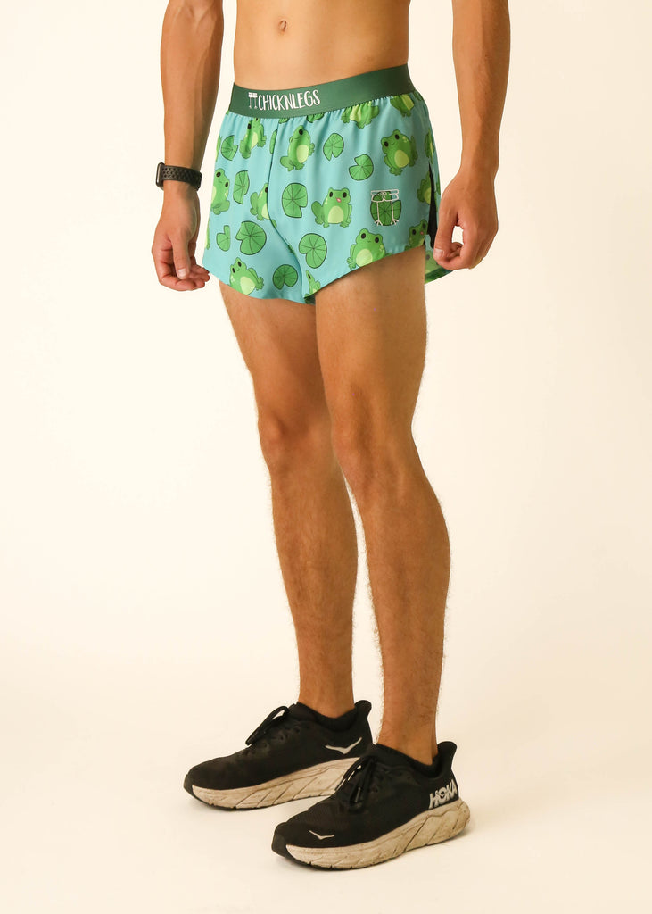 Model is a runner wearing athletic shorts made by Chicknlegs in the men's 2 inch split running shorts in the Fartlek Froggies Frog design, facing left.
