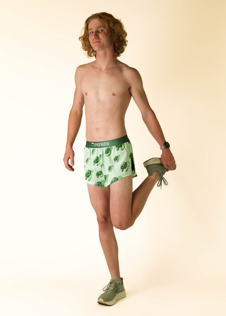 Model wearing Chicknlegs men's 2 inch split running shorts wearing the sea turtles posing while stretching their quad.
