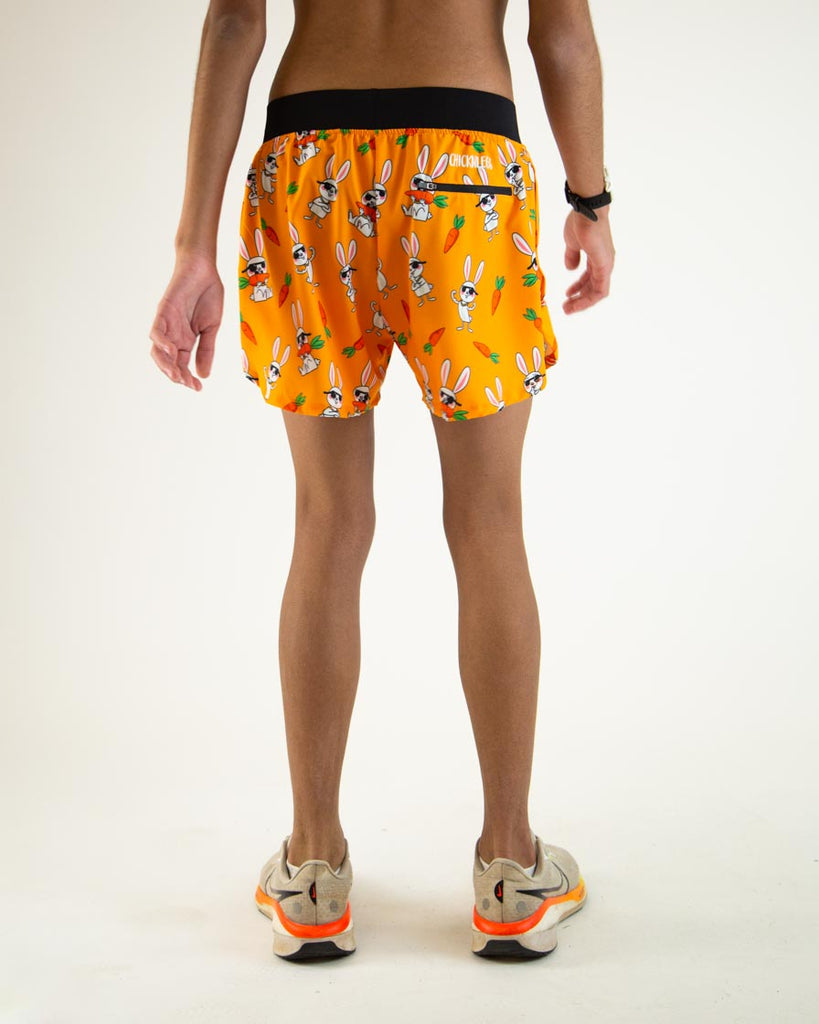 Runner is wearing ChicknLegs in the men's 4 in split running shorts in the bad bunny design, facing away from the camera. The print has white cute rabbits on it with sunglasses and carrots on an orange background. The shorts also have a back zipper pocket.