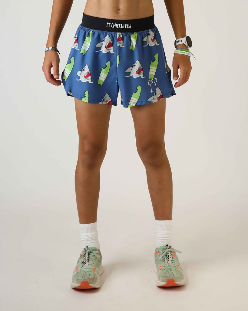 Runner is wearing ChicknLegs in the men's 4 in split running shorts that has a back pocket and inner liner pocket. The print has grey gray sharks on it with green surfboards on a blue background.