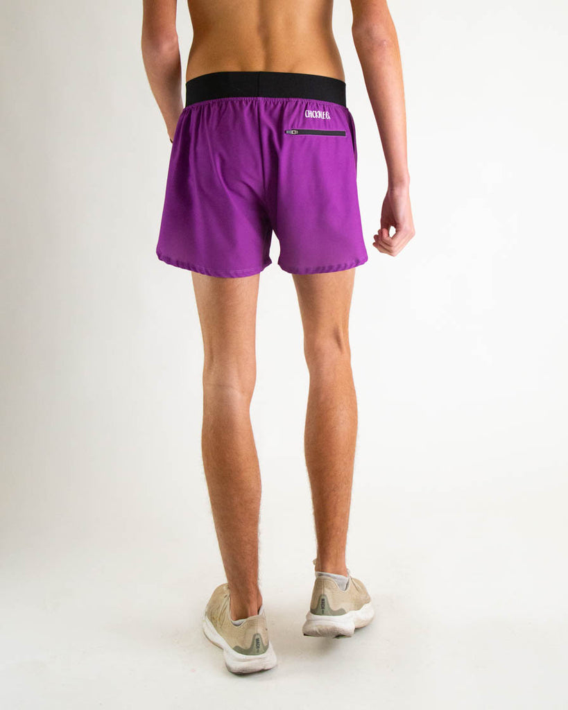 Runner is wearing ChicknLegs in the men's 4 in split running shorts with a back zipper pocket in the deep purple color facing away from the camera to show the back where the pocket is at.