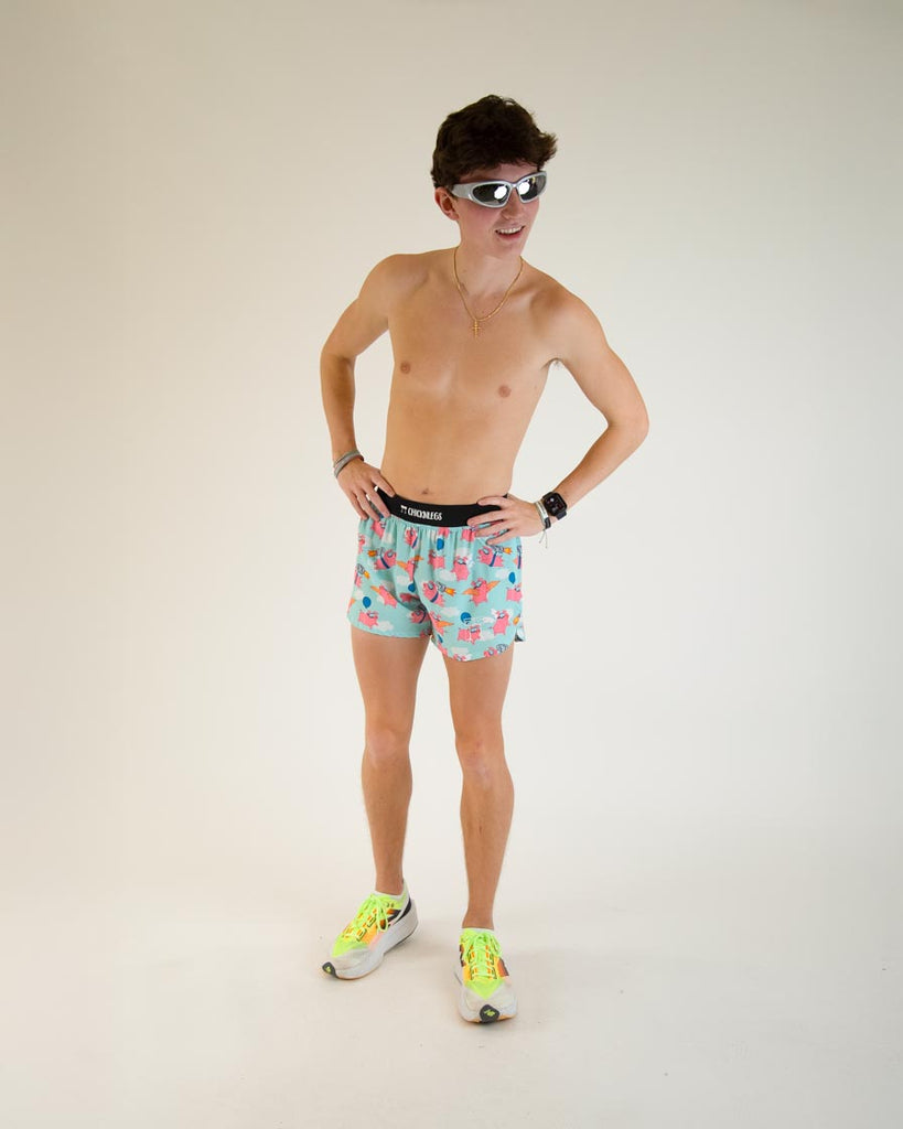 Runner is wearing ChicknLegs in the men's 4 in split running shorts in the flying pigs design, facing front. The print has pink flying pig on it with clouds, balloons, cardboard wings, and a jetpack and posing with funky fun 80s 70s 60s sunglasses.