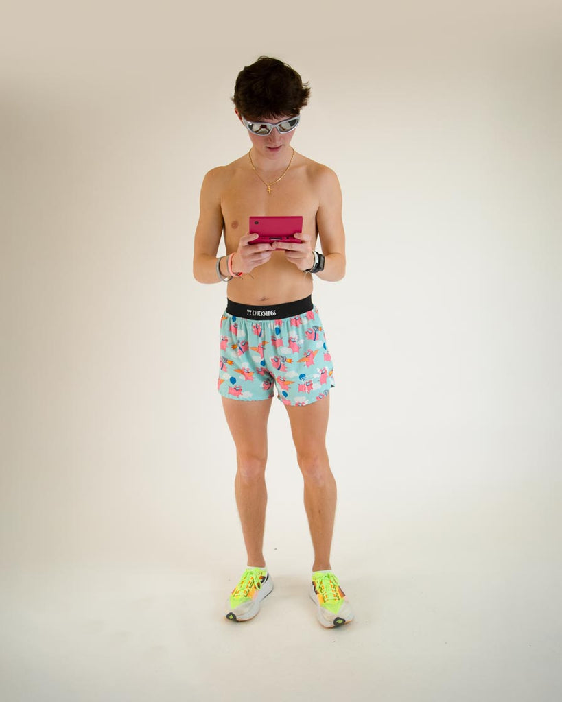 Runner is wearing ChicknLegs in the men's 4 in split running shorts in the flying pigs design, facing front. The print has pink flying pig on it with clouds, balloons, cardboard wings, and a jetpack, posing with fun devices for the smart science pig.