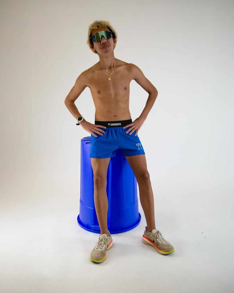 Runner is wearing ChicknLegs in the men's 4 in split running shorts in the royal blue design. The runner is posing with sunglasses and a giant blue recycle bin.