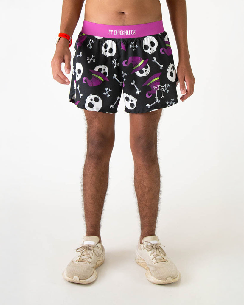 Runner is wearing ChicknLegs in the men's 4 in split running shorts in the skulls design. The print has skeleton skulls on it with bones and witch hats that are in white, purple and green on a black background.