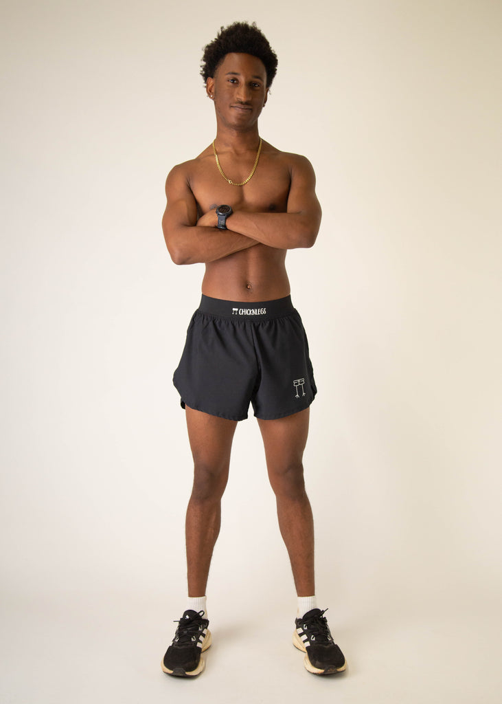 Model wearing Chicknlegs in mens 4 inch split running shorts in the black design, facing front while posing and crossing arms.