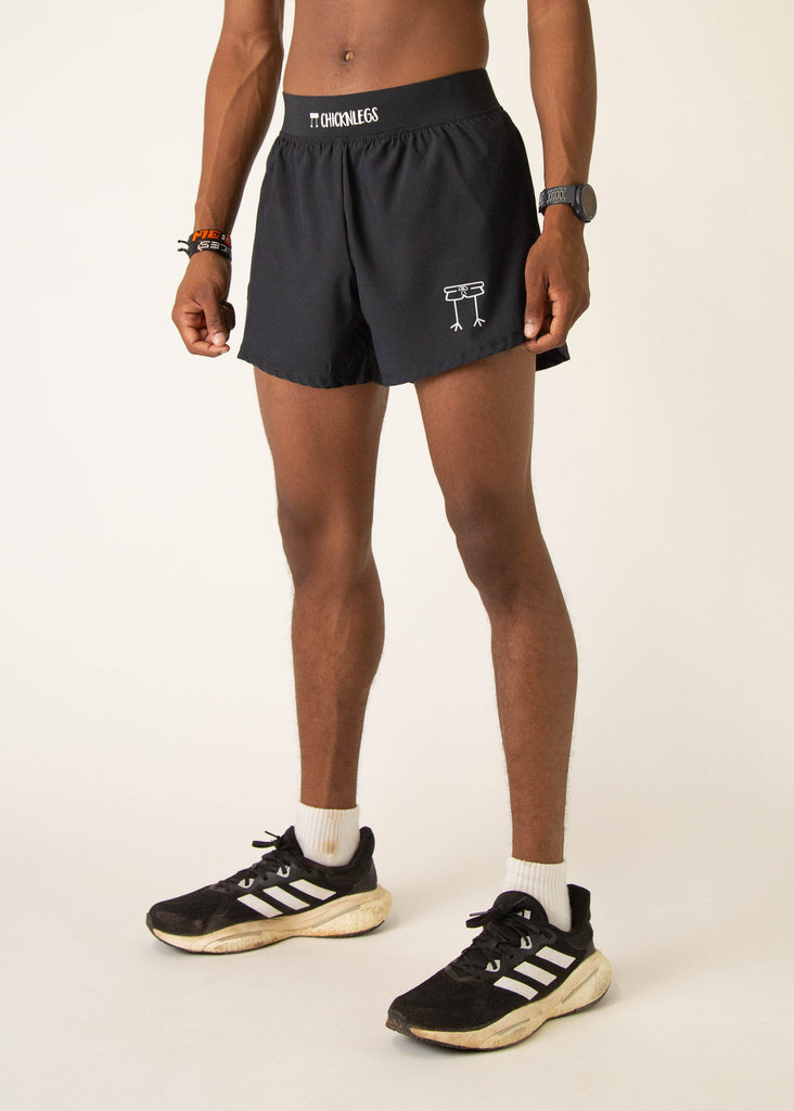 Model wearing Chicknlegs in mens 4 inch split running shorts in the black design, facing left.

