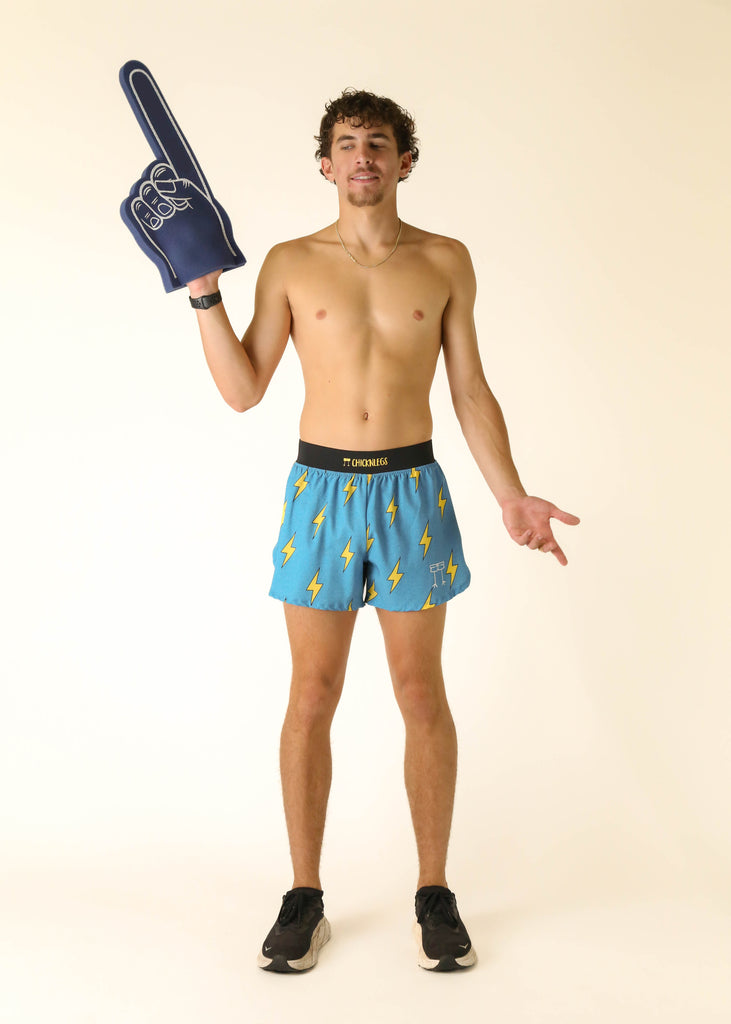 Model wearing Chicknlegs men's 4 inch split running shorts in the blue bolts design posing with blue foam finger.