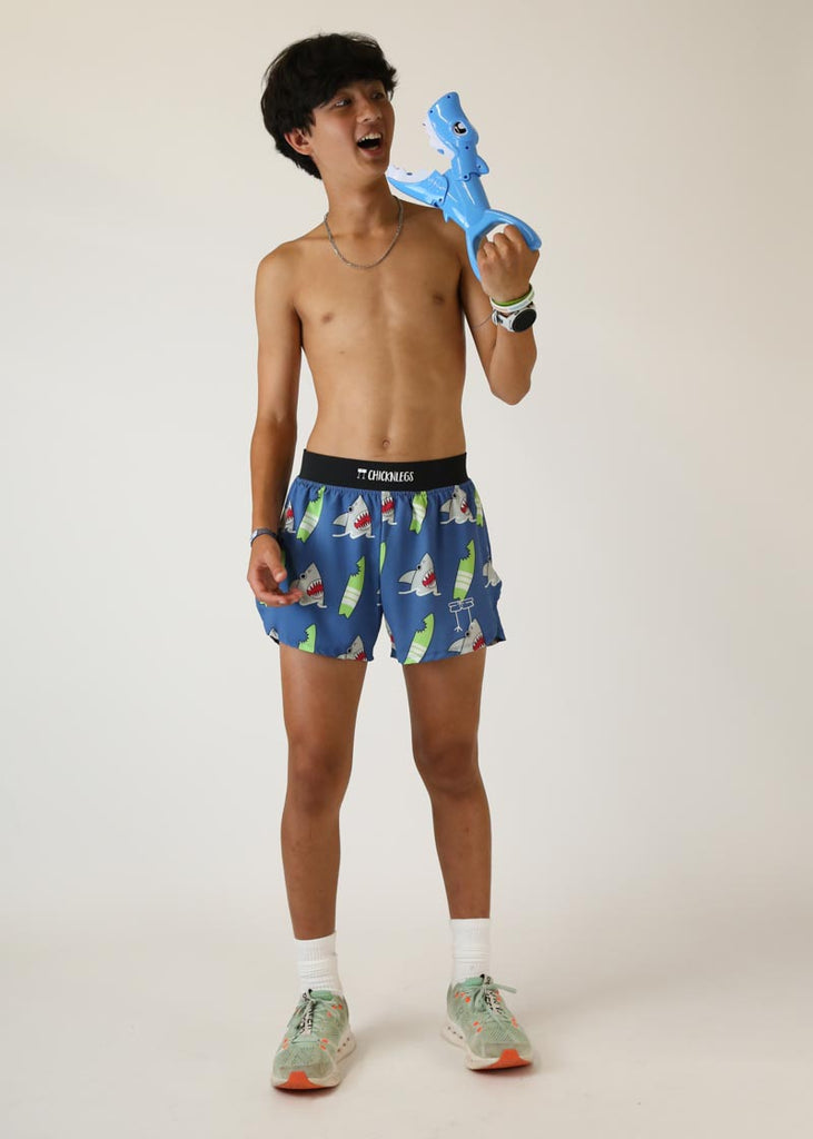 Model wearing Chicknlegs men's 4 inch split running shorts blue shark design holding shark toy