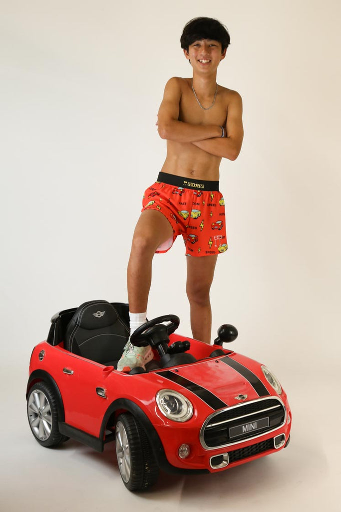 Model wearing Chicknlegs men's 4 inch split running shorts cars design posing with toy car