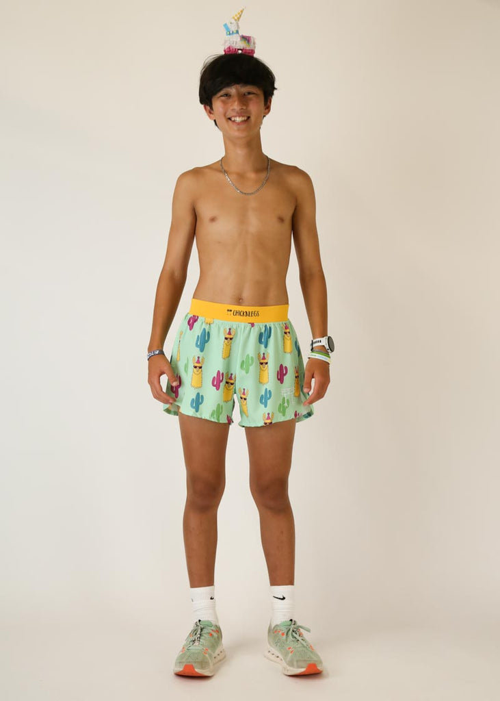 Model wearing Chicknlegs men's 4 inch split running shorts green llama design posing with llama pinata