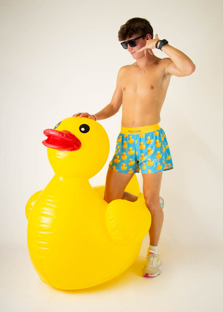 The model is a runner wearing Chicknlegs in the men's 4 inch split running shorts in the rubber ducky design, facing front while posing with a giant duck.