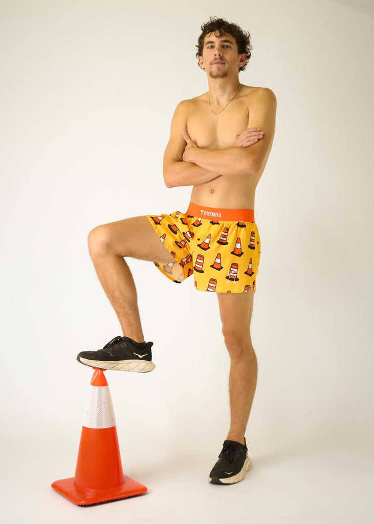 Model is a runner wearing Chicknlegs men's 4 inch split running shorts in the traffic cones design, facing front while posing with a traffic cone.