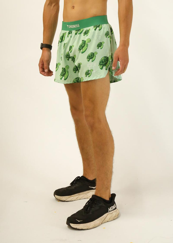Model is a runner who is wearing Chicknlegs men's 4 inch split running shorts in the turtles design, facing left.