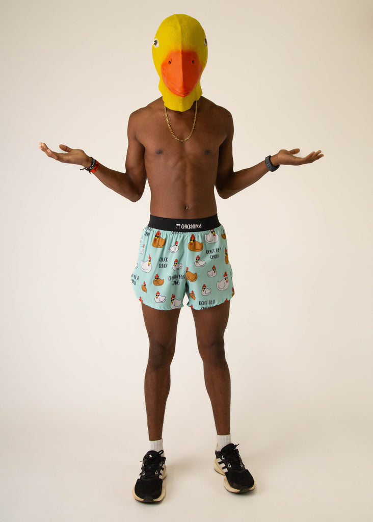 Model wearing Chicknlegs in mens 4 inch split running shorts in the swaggy chickns design, facing front while posing with giant chicken mask.
