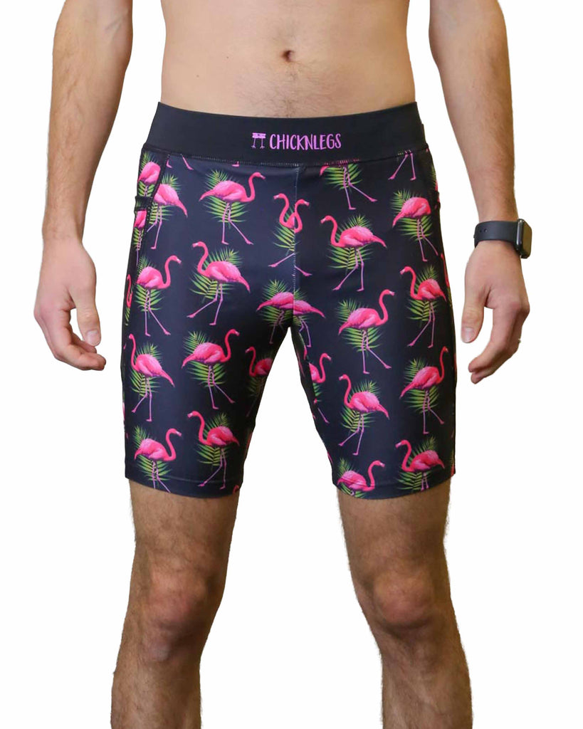 Runner is wearing ChicknLegs in the men's 8 in half tights with pockets in the flamingo design. The print has fun pink flamingos on it with green leaves on a solid black background.