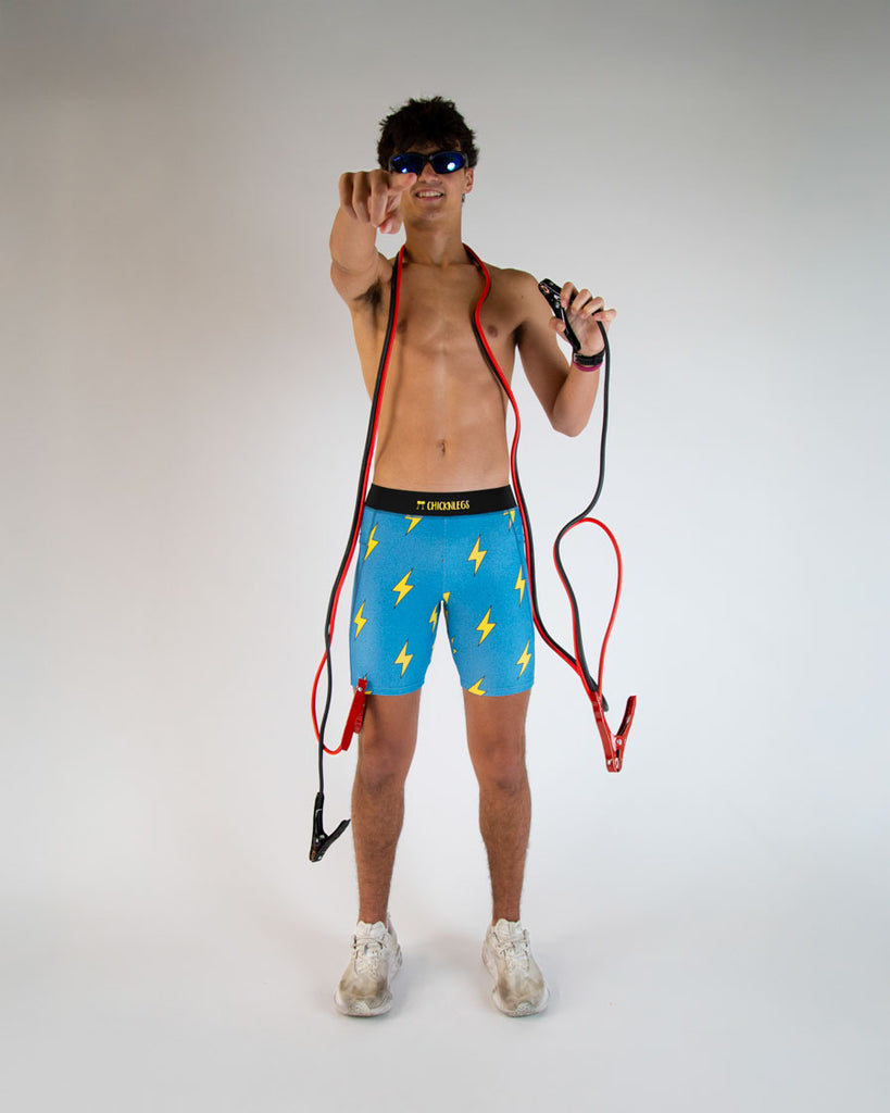 Runner is wearing ChicknLegs in the men's 8 in half tights in the blue bolts design. The print has yellow lightning bolts on a blue background. The runner is holding car plugs to help with electricity. 