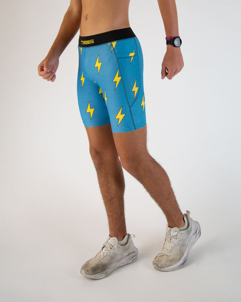 Runner is wearing ChicknLegs in the men's 8 in half tights in the blue bolts design. The print has yellow lightning bolts on a blue background. The sides have iphone and android size pockets made for running, hiking, track and field, surfing, working out and weight lifting.