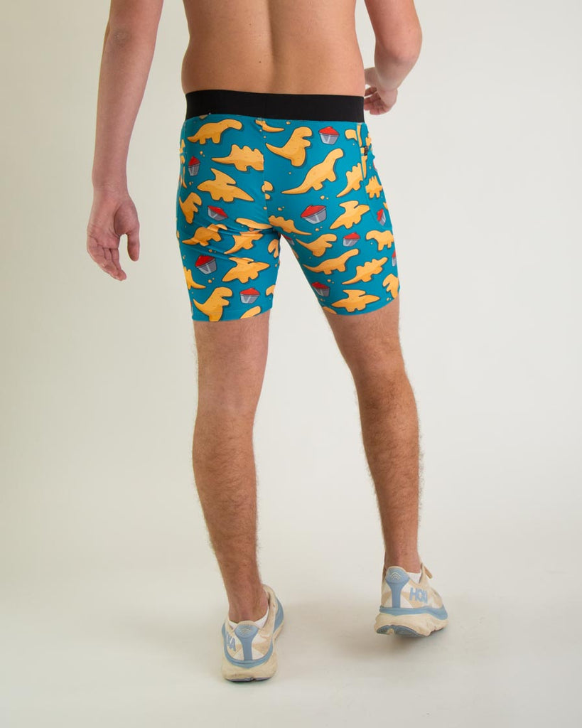 Runner is wearing ChicknLegs in the men's 8 in half tights with pockets in the dino nugget design. The print has chicken dinosaur nuggets on it with ketchup in an orange, red and blue color. A back view of the halftights are shown, great for long distance running and performance to prevent chaffing.  
