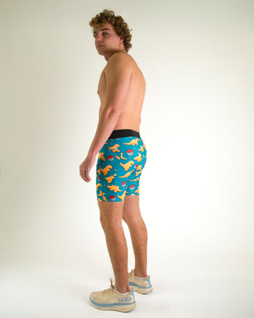 Runner is wearing ChicknLegs in the men's 8 in half tights with pockets in the dino nugget design. The print has chicken dinosaur nuggets on it with ketchup in an orange, red and blue color. A full body view of the halftights are shown, great for long distance running and performance to prevent chaffing.  