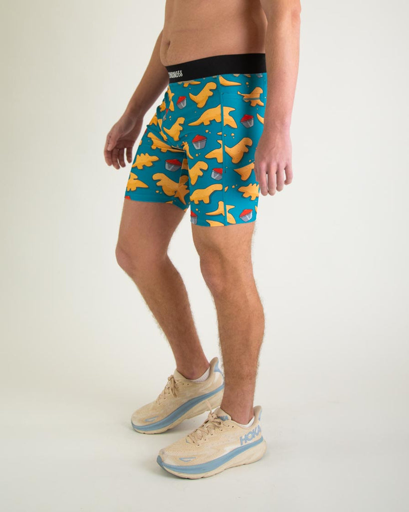 Runner is wearing ChicknLegs in the men's 8 in half tights with pockets in the dino nugget design. The print has chicken dinosaur nuggets on it with ketchup in an orange, red and blue color. A left view of the halftights are shown, great for long distance running and performance to prevent chaffing.  