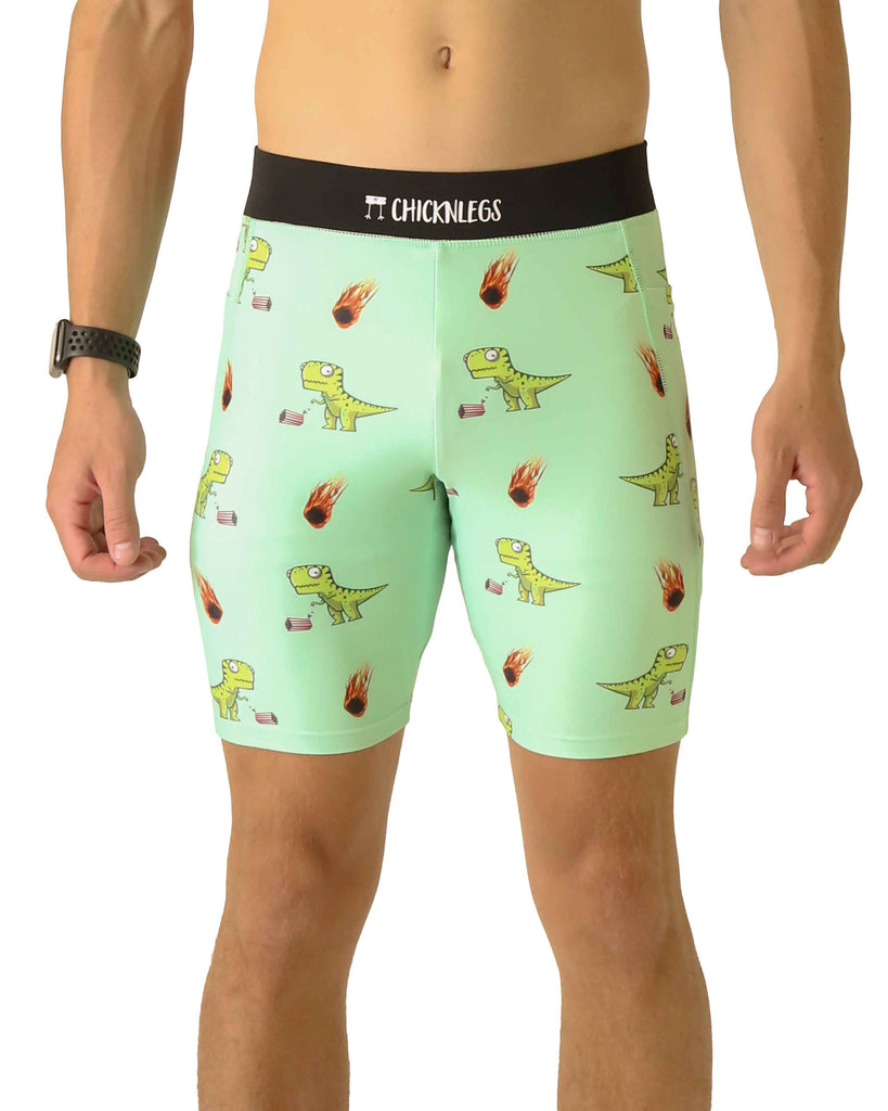 Runner is wearing ChicknLegs in the men's 8 in half tights with pockets in the dino-sore design. The print has green dinosaurs on it with popcorn and a meteor, on a light green solid color background.