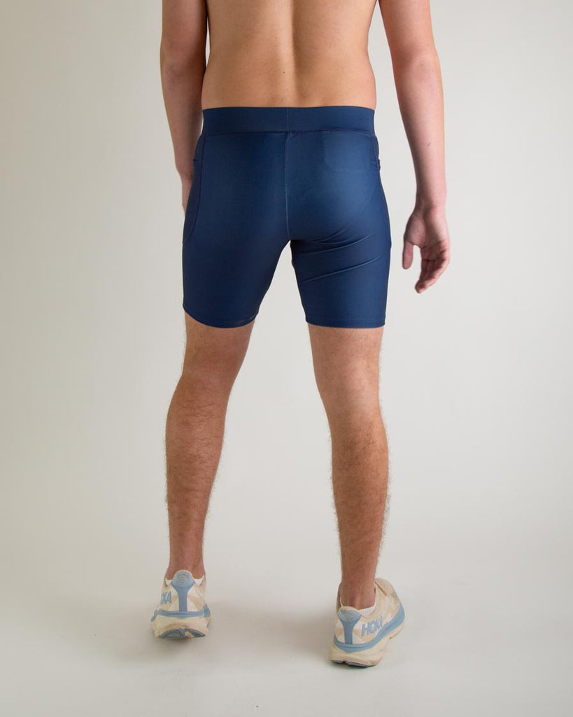 Runner is wearing ChicknLegs in the men's 8 in half tights with pockets in the navy design. The print is a solid navy blue color, great to protect from chaffing and long runs, a back view is shown.
