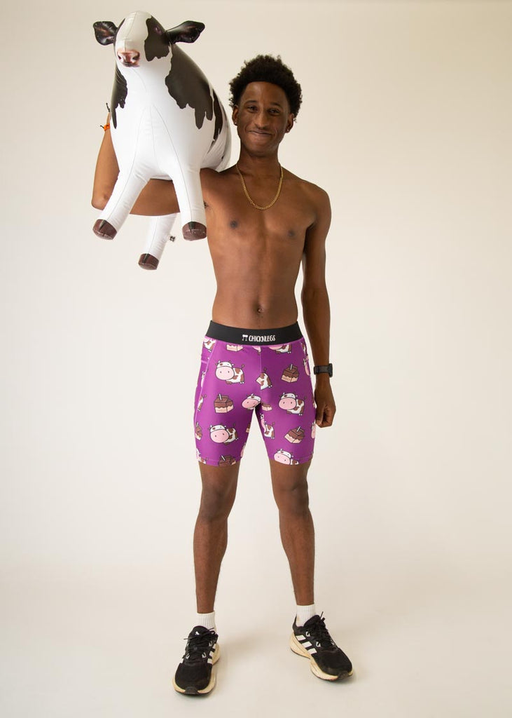 Model wearing Chicknlegs men's 8 inch half tights in the choccy cow design, facing front and posing while holding a cow.