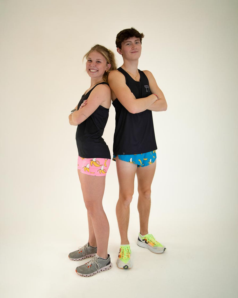 Runner is wearing ChicknLegs in the women's performance singlet in the solid black design. Another model is shown wearing a black singlet and wearing blue banana shorts in the men's 2 in split shorts.