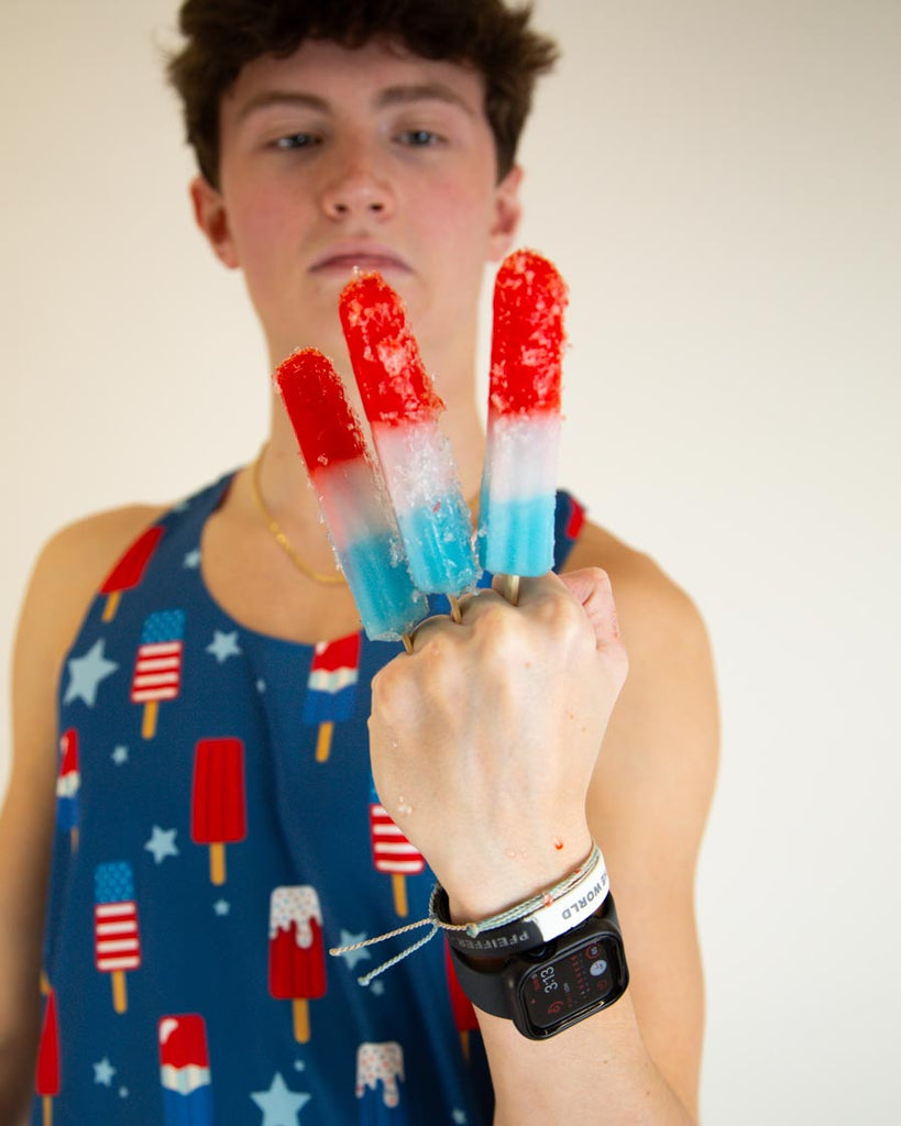 Runner is wearing ChicknLegs men's performance singlet in the USA Popsicle design, facing front. The print has red, white and blue ice cream on it with stars and melting ice cream.