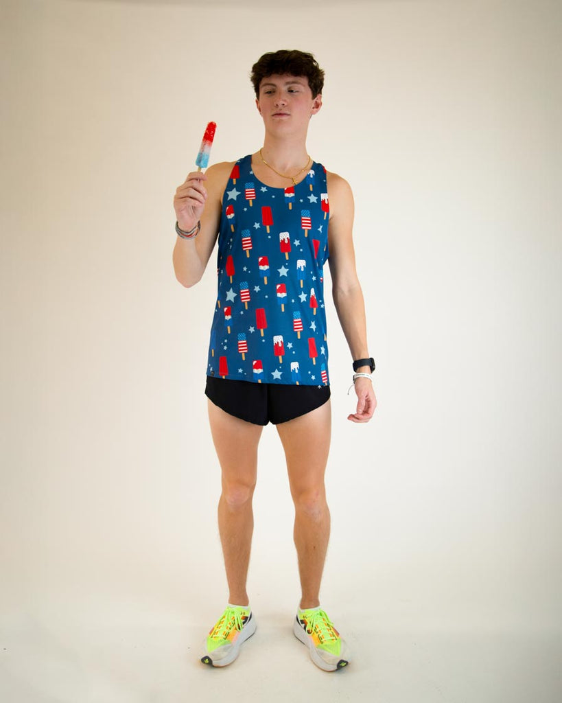 Runner is wearing ChicknLegs men's performance singlet in the USA Popsicle design, facing front. The print has red, white and blue ice cream on it with stars full body pose while eating ice cream.