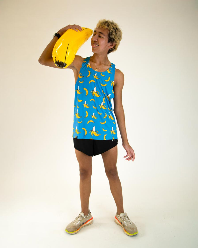 Runner is wearing ChicknLegs men's performance singlet in the blue banana design. A full body image is shown of the outfit whole holding a giant banana.