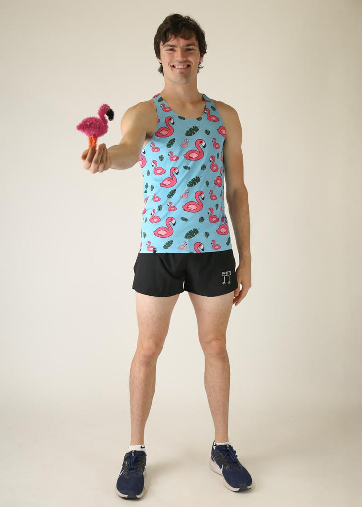 Model wearing chicknlegs men's performance singlet in wearing blue flamingo design full body view posing with little flamingo.