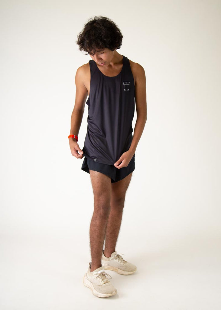 The model is a runner who is wearing Chicknlegs men's running performance singlet in the black design, posing while holding the singlet.