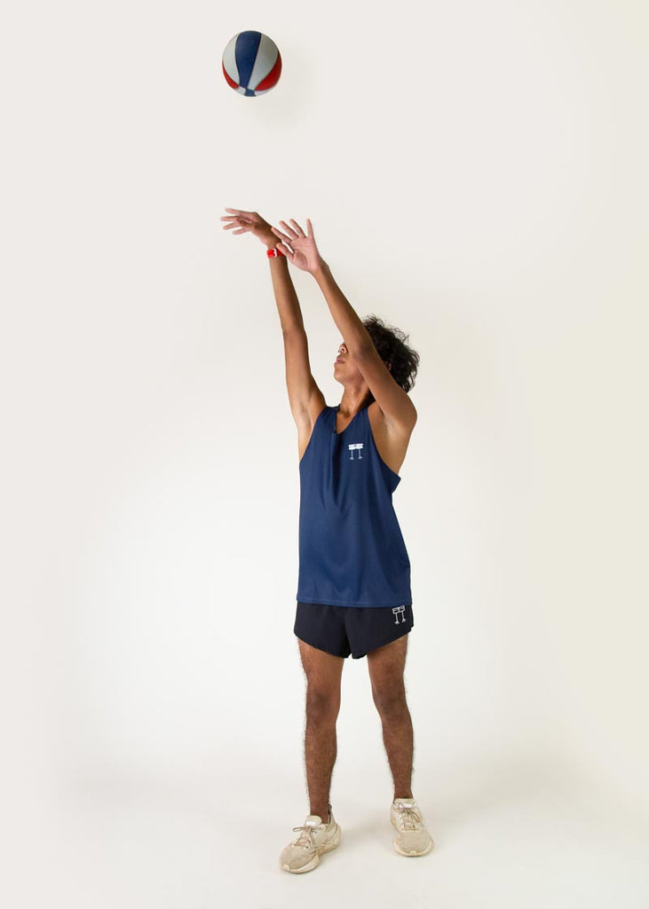 The model is a runner who is wearing Chicknlegs men's running performance singlet in the navy design, posing with a basket ball jumping and tossing the ball up into the air.