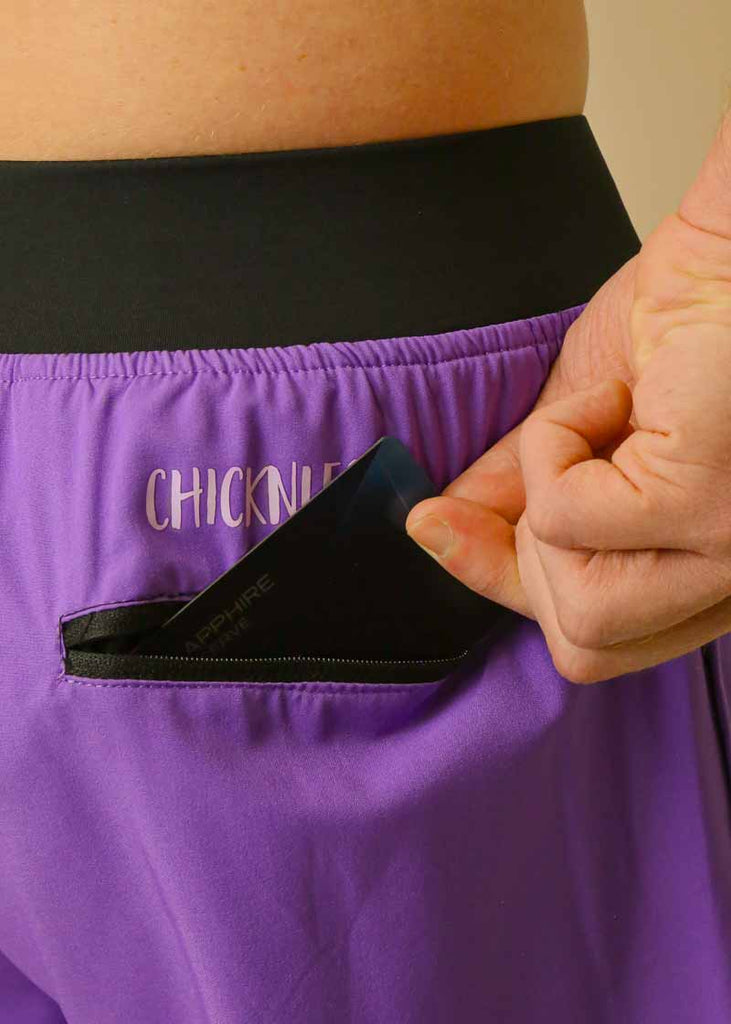 Model is wearing the men's 4 inch running shorts from the brand Chicknlegs, reaching into the back pocket to grab a card.