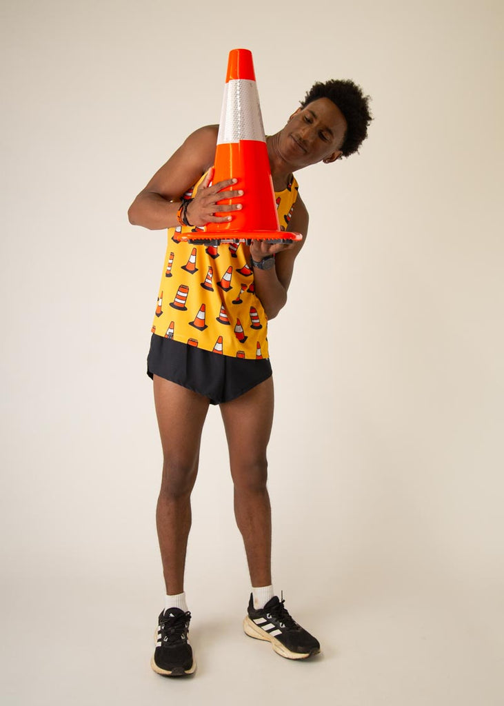 Model is wearing Chicknlegs men's runner singlet in the Traffic Cones design, facing front while posing with a traffic cone in front of him.