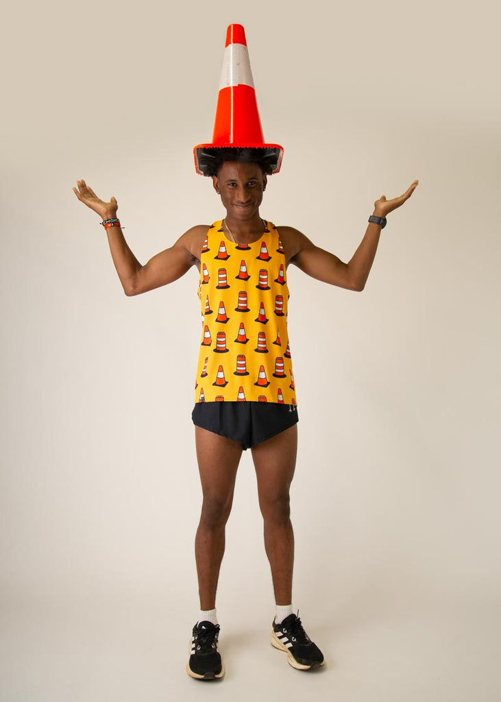 Model is wearing Chicknlegs men's runner singlet in the Traffic Cones design, facing  front while posing with a traffic cone on their head.