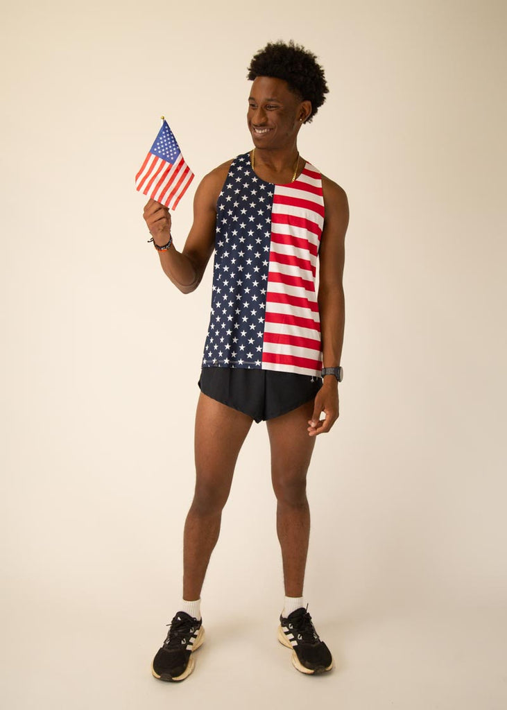 Model is wearing Chicknlegs men's runner singlet in the USA design, facing front while posing with the USA flag.