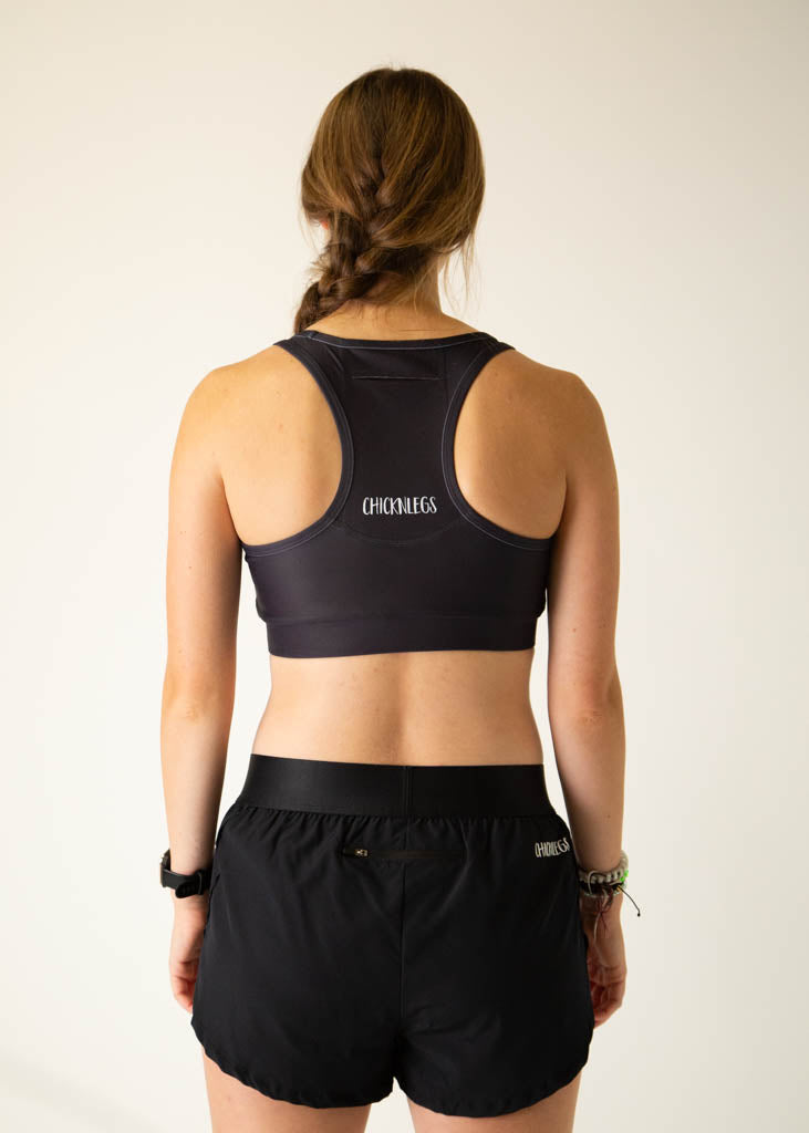 The model is a runner wearing Chicknlegs women's OG sports bra in the black design, facing away from the camera to show the back of the sports bra. It includes a pocket.