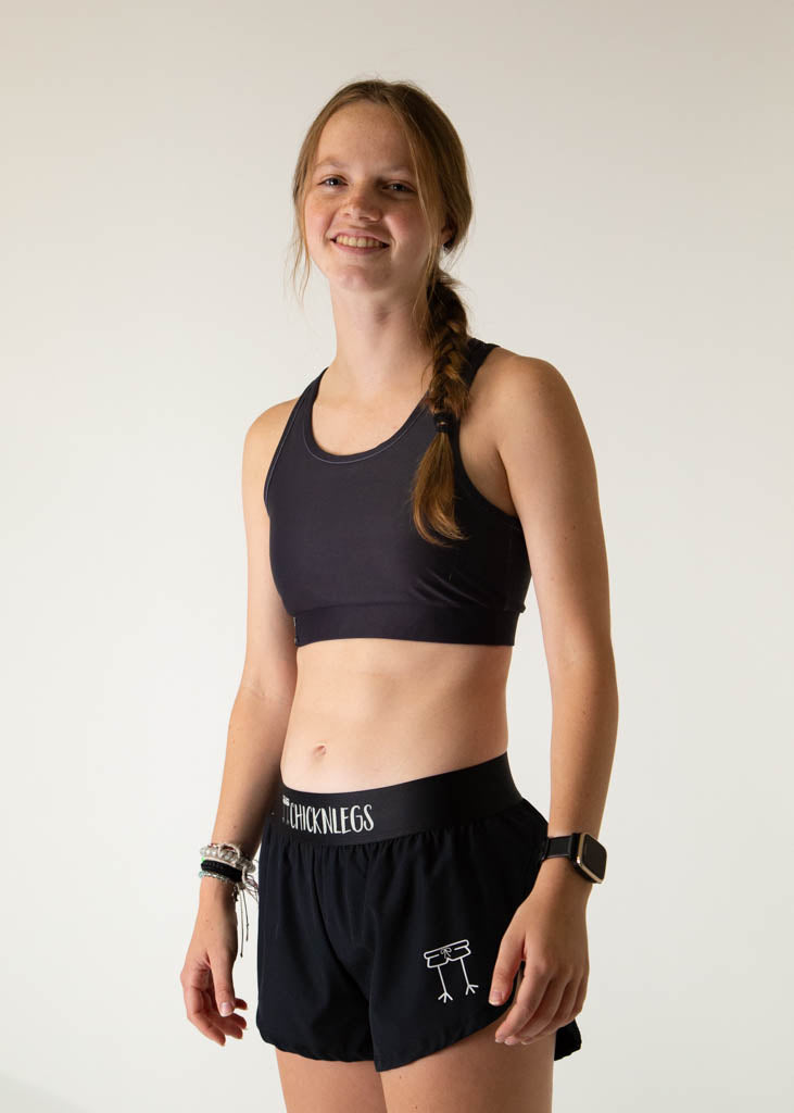 The model is a runner wearing Chicknlegs women's OG sports bra in the black design, facing left.