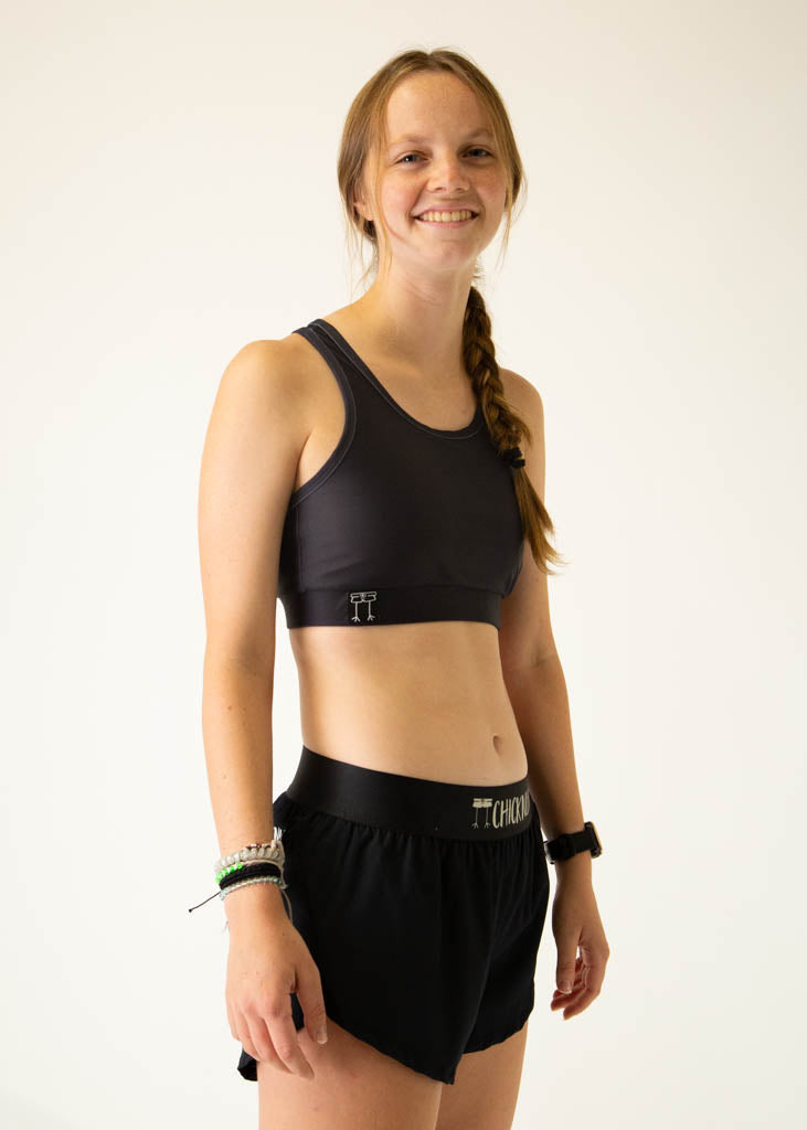 The model is a runner wearing Chicknlegs women's OG sports bra in the black design, facing right.