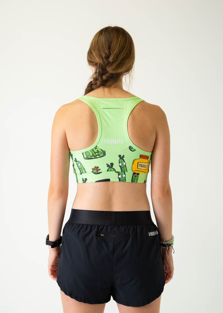 The model is a runner who is wearing Chicknlegs women's OG sports bra in the pickles design, facing away from the camera to show the back of the sports bra, a pocket is included.