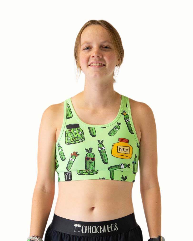 Runner is wearing ChicknLegs in the women's OG Sports Bra has a back pocket for exercise, running, workout, gym, and every day lifestyle. The print is the pickles design which has green pickles in different shapes and sizes and a green and yellow jars.