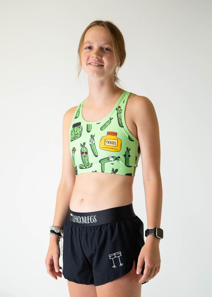 The model is a runner who is wearing Chicknlegs women's OG sports bra in the pickles design, facing left.
