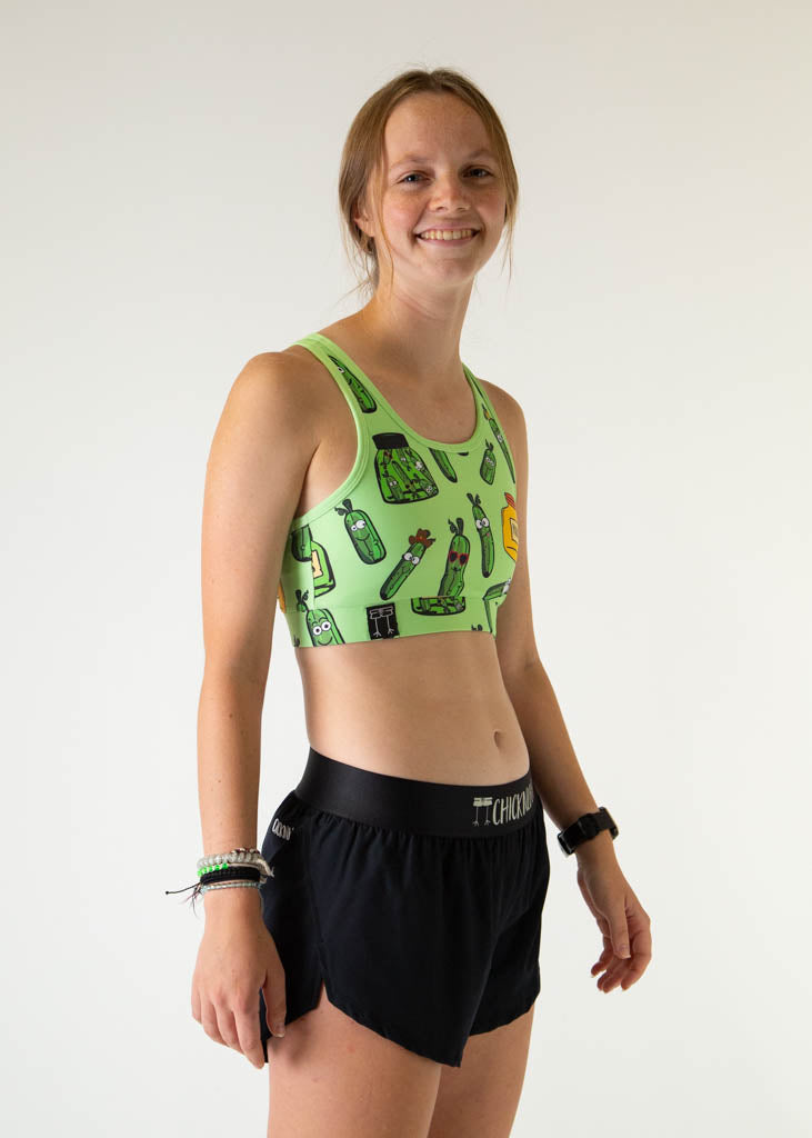 The model is a runner who is wearing Chicknlegs women's OG sports bra in the pickles design, facing right.