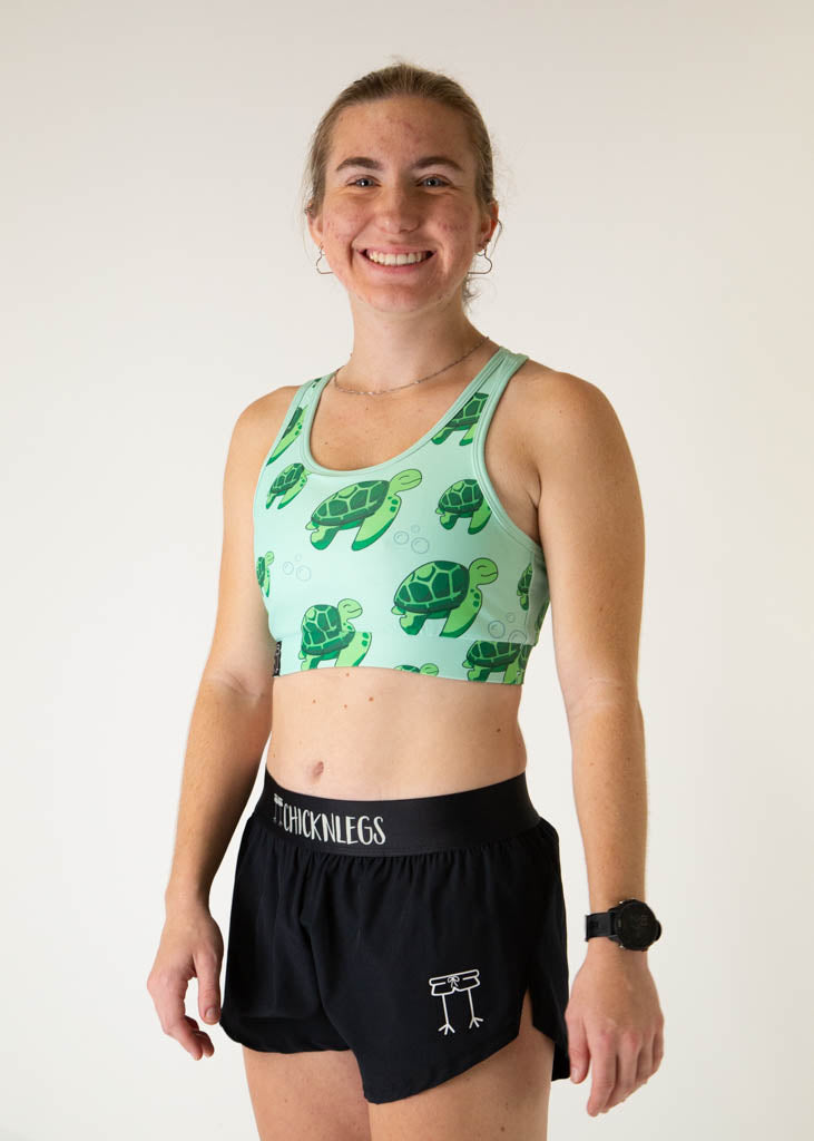 The model is a runner who is wearing Chicknlegs OG sports bra in the turtles design, facing left.