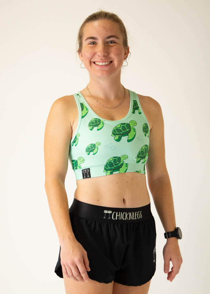 The model is a runner who is wearing Chicknlegs OG sports bra in the turtles design, facing right.