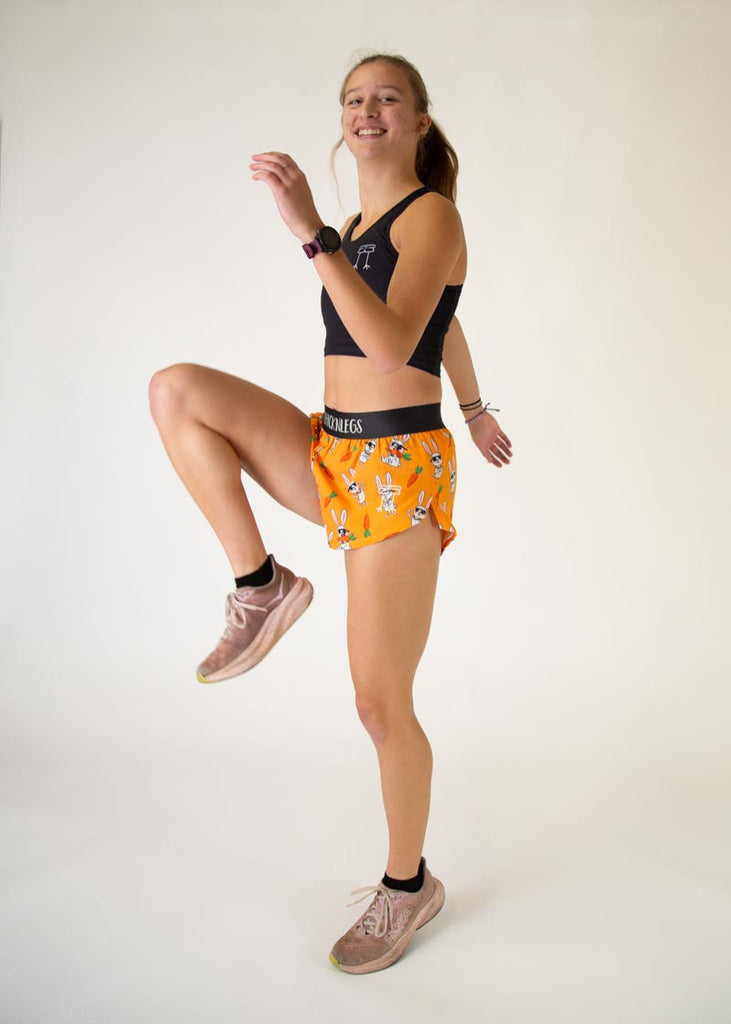 Runner is wearing ChicknLegs in the women's 1.5 in split running shorts with the bad bunny design. The print has white rabbits on it with sunglasses and carrots. The model is in a running high leg pose.