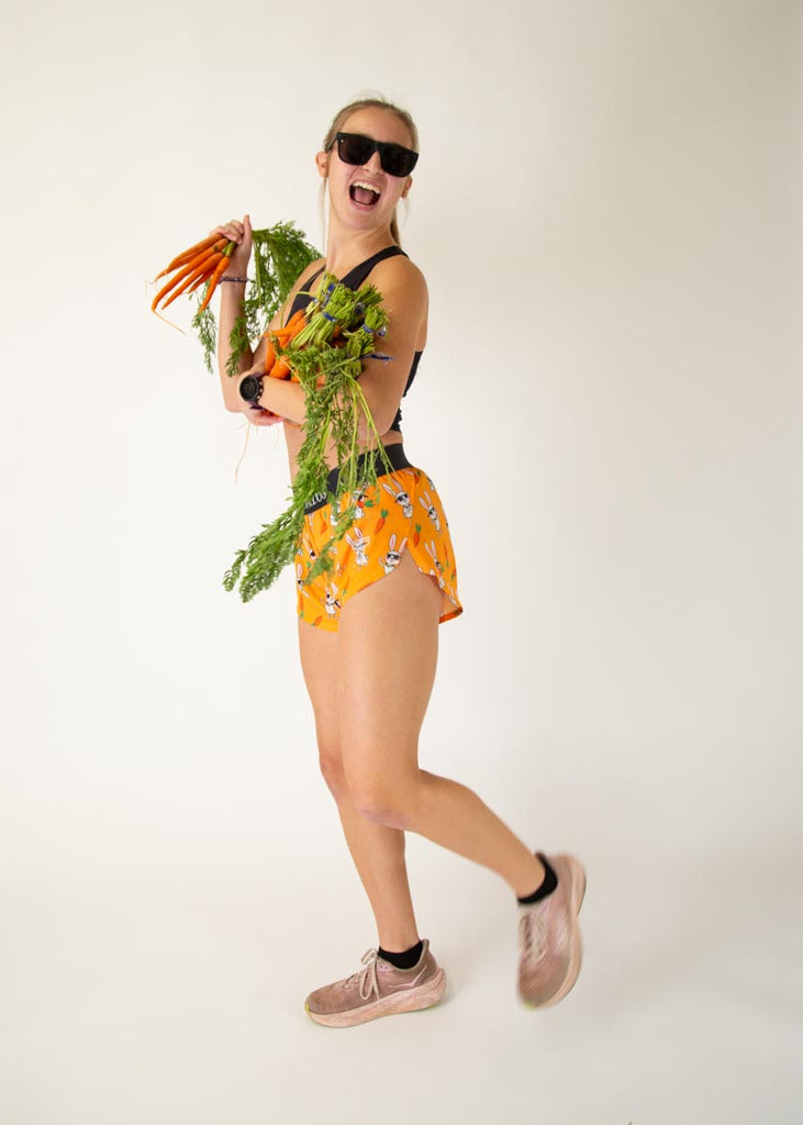 Runner is wearing ChicknLegs in the women's 1.5 in split running shorts with the bad bunny design. The print has white rabbits on it with sunglasses and carrots, posing with sunglasses and real carrots.